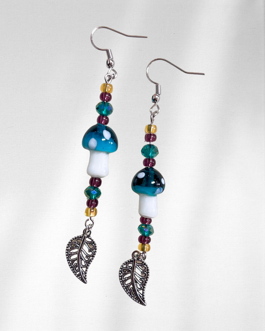 Pair of mushroom-shaped beaded earrings with leaf charms on a white background