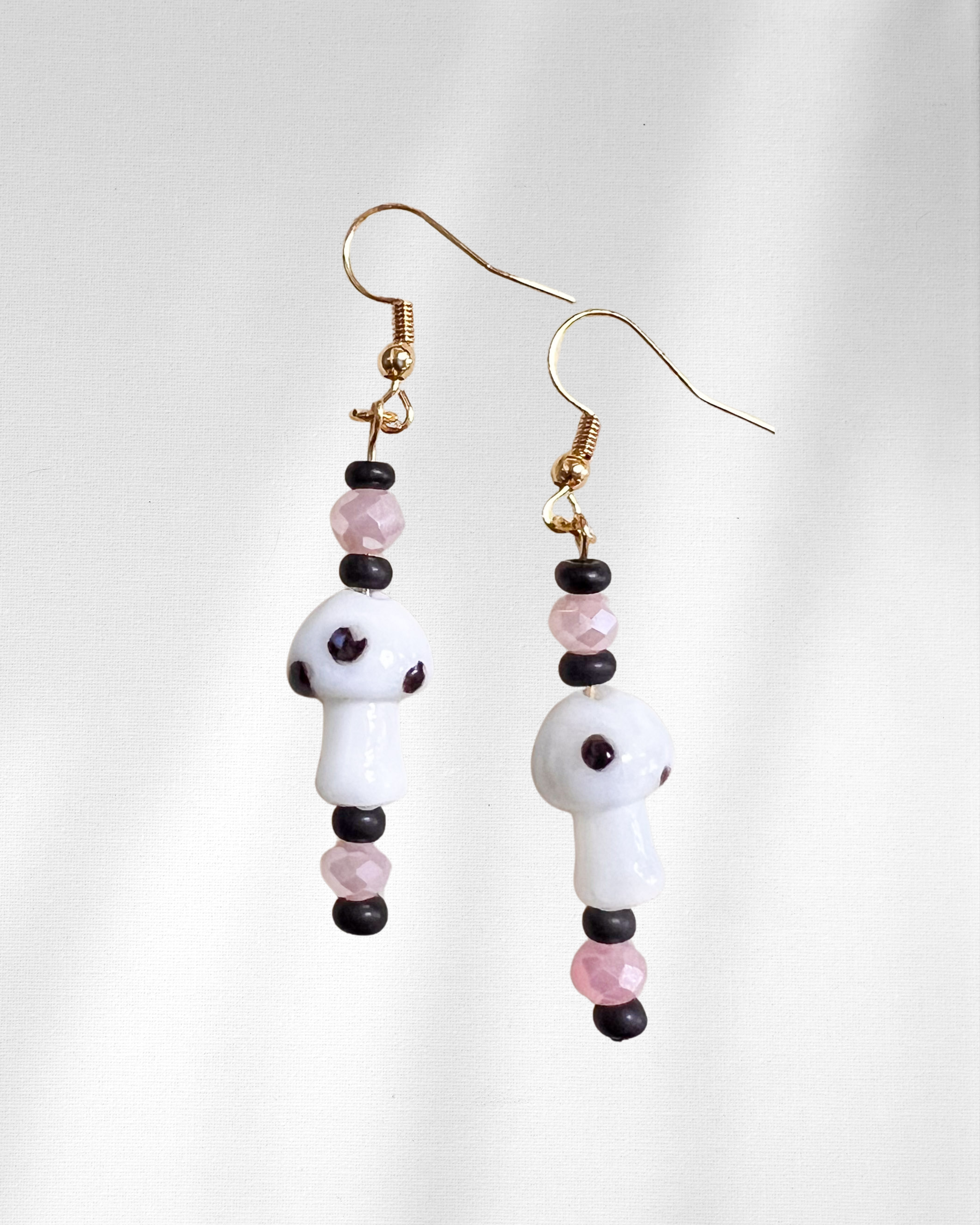 Pair of beaded earrings with white glass mushroom charms, white, pink, and black beads on a light gray background