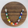 A necklace with multicolored glass mushroom charms on a gold plated chain, displayed on a wooden round stand.