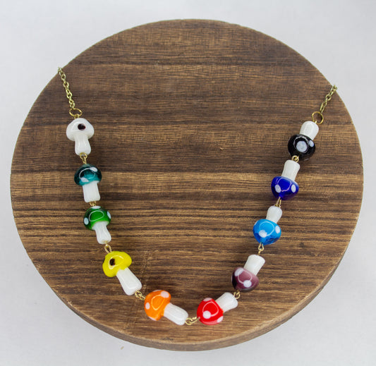 A necklace with multicolored glass mushroom charms on a gold plated chain, displayed on a wooden round stand.